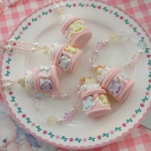 Sweet Lolita carousel macaron resin necklace and bag pendant collection displayed on floral porcelain plate with pink gingham tablecloth, featuring assorted pastel colored macaron charms with cream toppings, pearl and crystal beaded chains