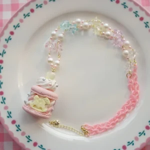 Single sweet Lolita carousel macaron pendant necklace close-up on floral-rimmed porcelain plate, showcasing detailed pink macaron charm with intricate carousel design, pink acrylic chain sections, pearl and crystal beads with gold-toned extender