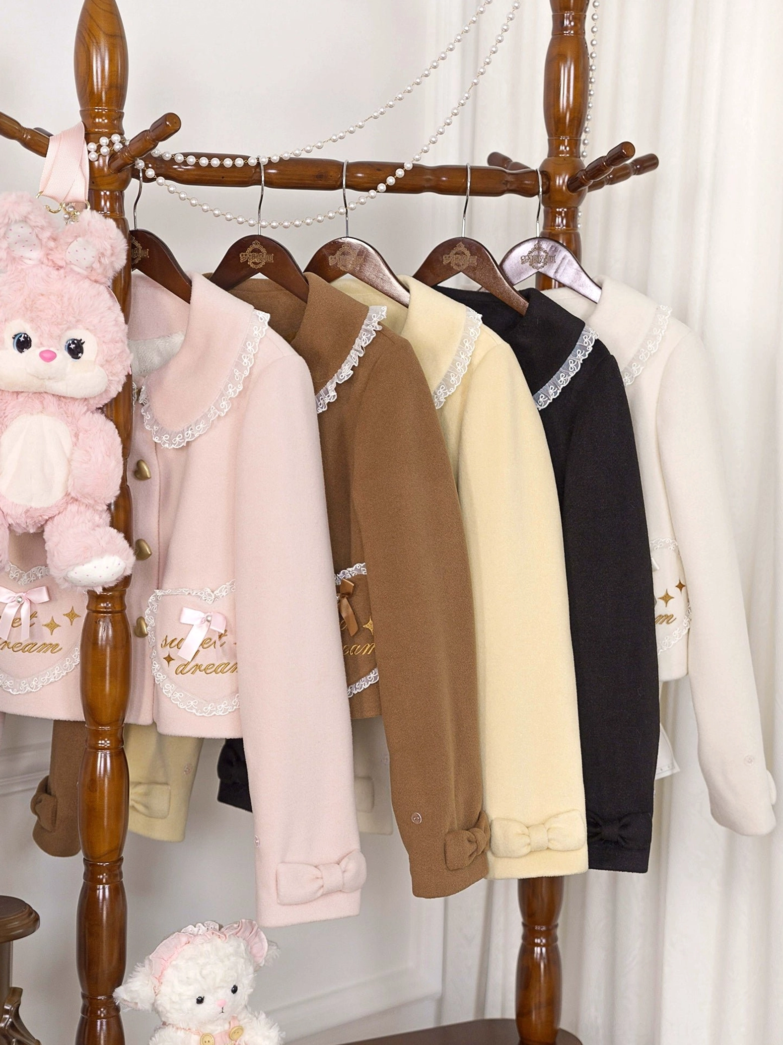 Sweet lolita coat collection featuring peter pan collar design and embroidered pocket details, shown hanging on vintage wooden clothing rack with doll props