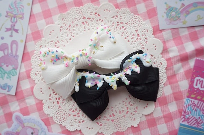 White and black handmade sweet lolita bow hair clips with cream drizzle and candy sprinkles on lace background flat lay