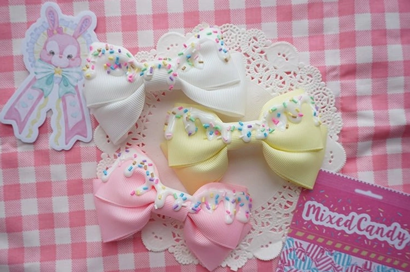 Three handmade sweet lolita bow hair clips in white yellow and pink with imitation cream and candy sprinkles on checkered background
