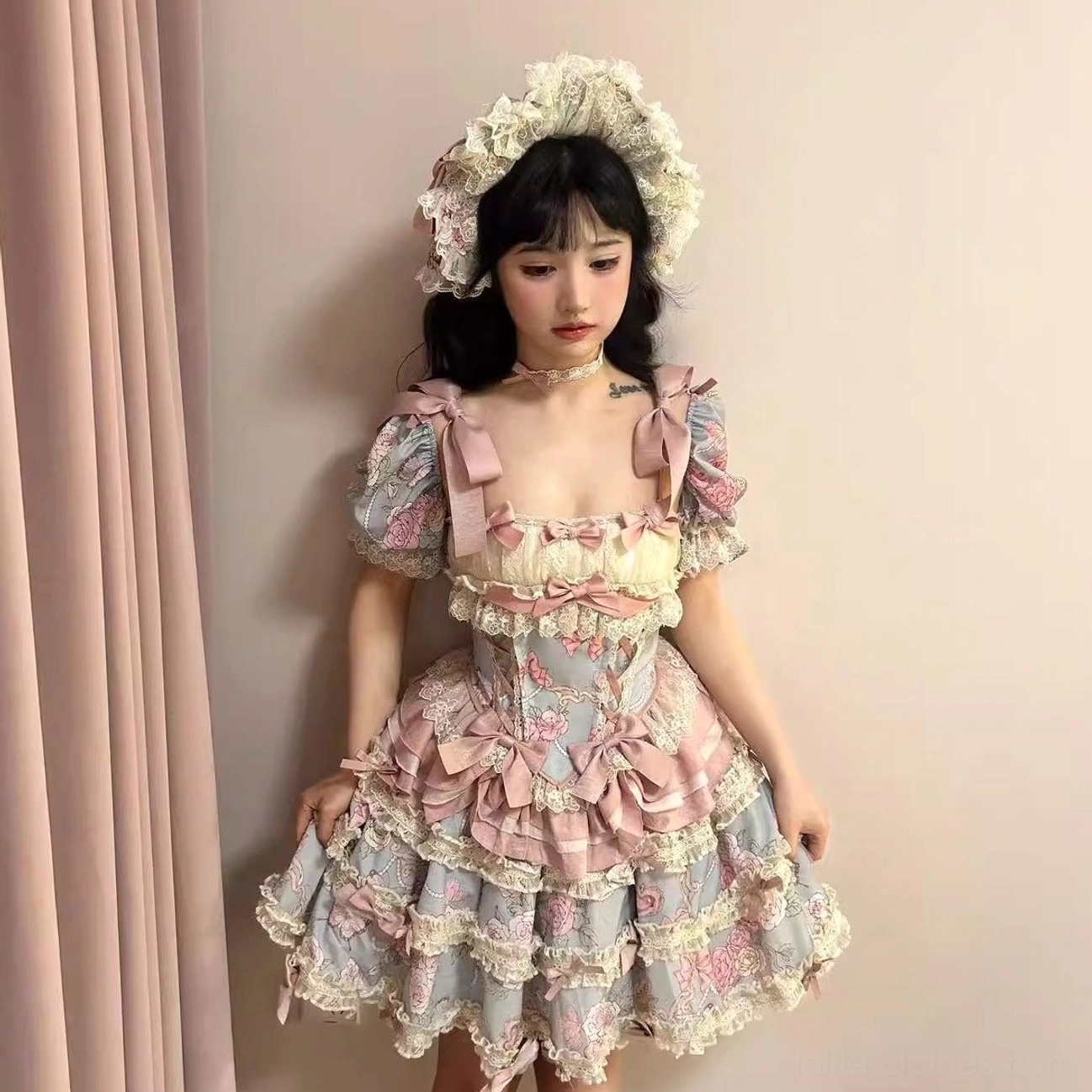 Three-quarter front view of short-style sweet lolita dress set with fitted corset bodice ruffle trim on neckline pink satin bow accents on model against pink curtain backdrop