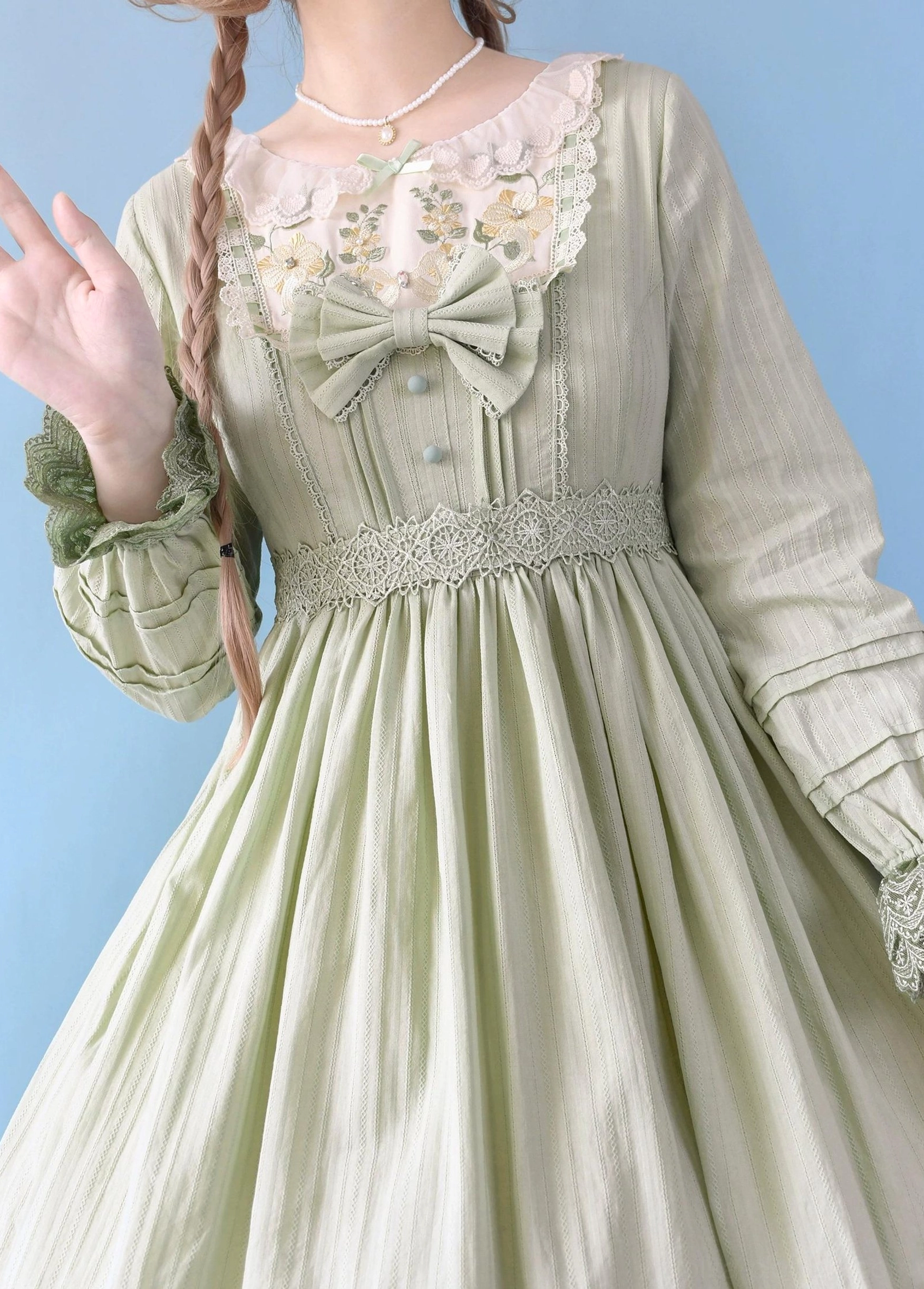 Sage green Sweet Lolita embroidered OP dress close-up upper body shot featuring long puff sleeves with ruffled cuffs, embroidered lace neckline, front big bow, waist lace trim, subtle stripe fabric