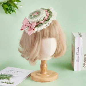 Sweet Lolita floral embroidery top hat with pink satin bow and white ruffled lace trim, worn on blonde mannequin displaying ornate round floral medallion with sage green accents