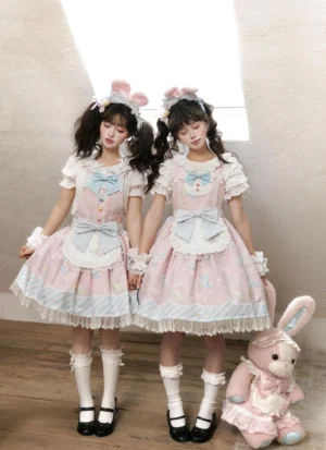 Front full-body view of sweet Lolita jumper skirt with bunny print worn by model on wooden studio floor, showcasing ruffled lace trims, front bowknots, and short lace-cuffed sleeves in pastel pink colorway