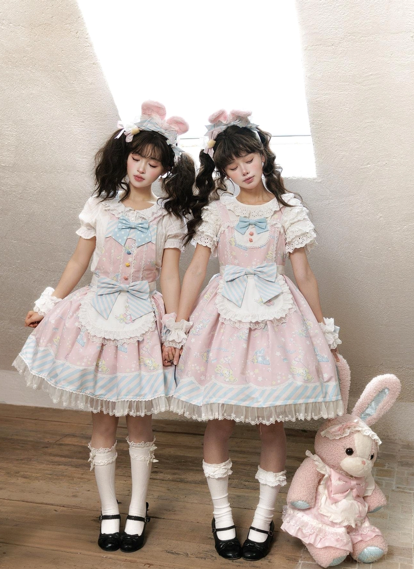 Front full-body view of sweet Lolita jumper skirt with bunny print worn by model on wooden studio floor, showcasing ruffled lace trims, front bowknots, and short lace-cuffed sleeves in pastel pink colorway