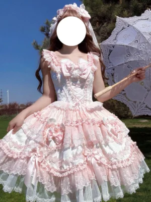 Sweet Lolita JSK dress front full-body view model wearing pink white ruffled lace jumper skirt with heart bow details paired with lace parasol bridal veil outdoor lawn