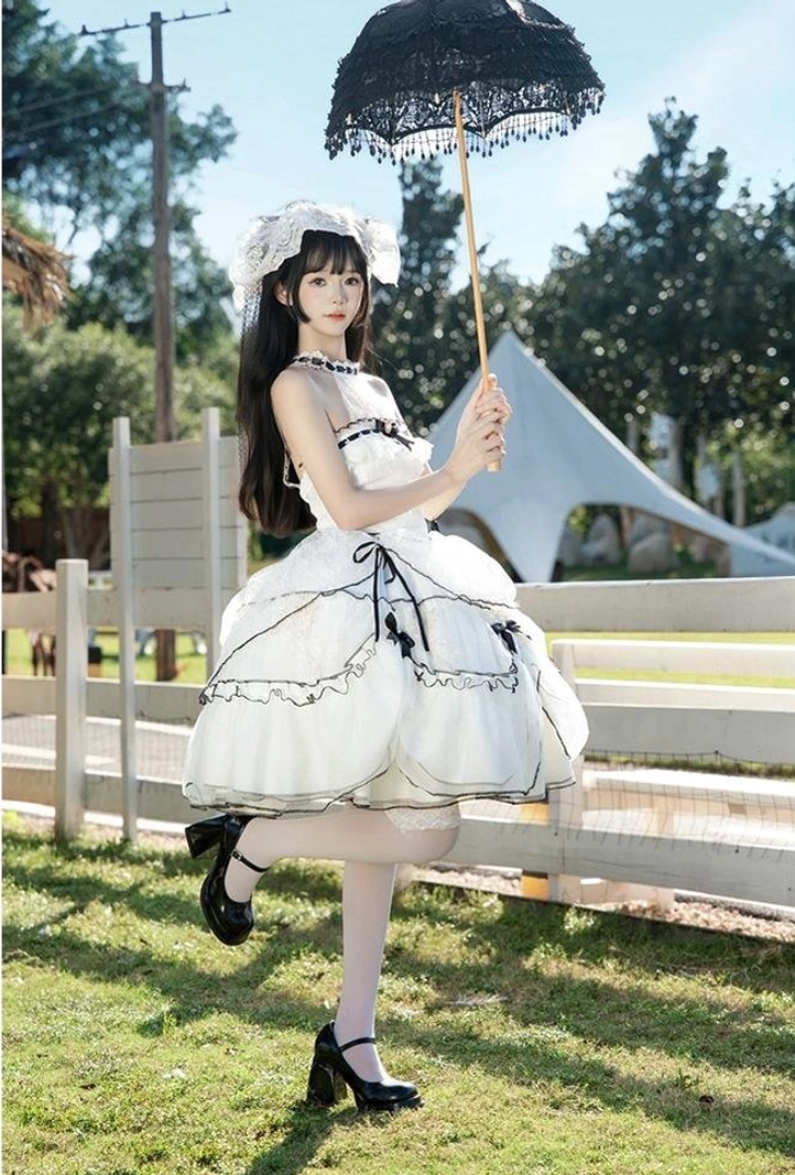 Side profile of model in wedding sweet lolita JSK dress with layered tulle skirt sitting on garden lawn wearing black Mary Jane heels and white stockings with lace accessories