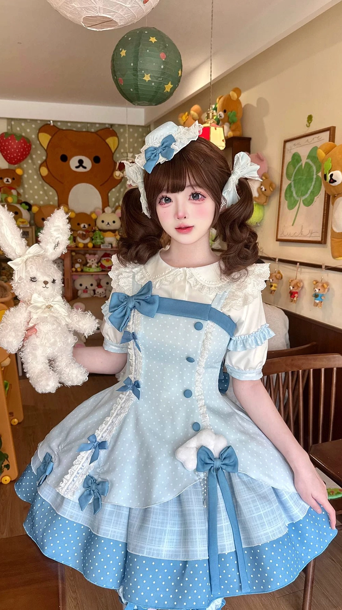 Sweet Lolita dress side-front full-body view worn by model with matching leg garters, blue hair accessories, holding plush rabbit, plush toy themed indoor space background