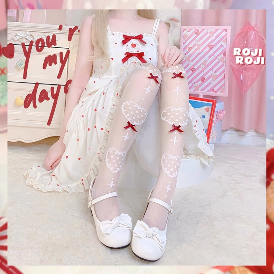 Lolita girl wearing ethereal nude sheer knee socks with red bow heart motifs paired with white bow Mary Jane shoes and white sweet Lolita dress in soft bedroom setting