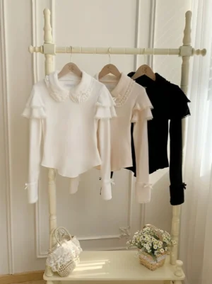 Front display view of white and black sweet lolita knit sweater with Peter Pan collar, lace trim, ruffled flutter sleeves, and decorative bow cuffs on clothing rack