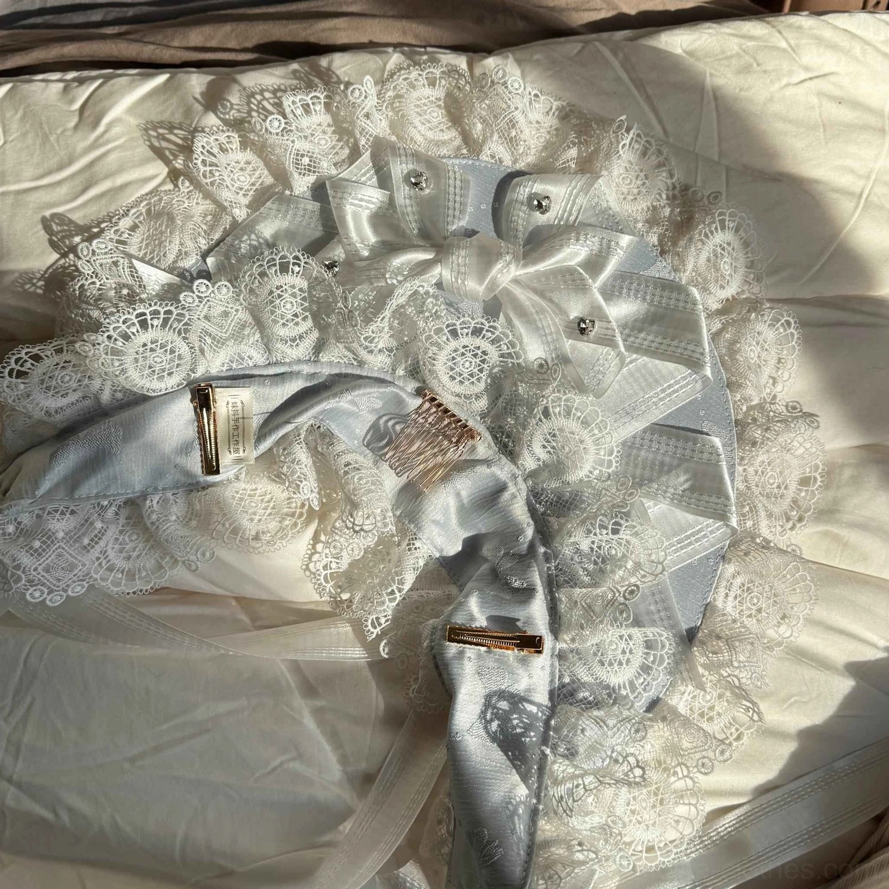 Sweet Lolita lace head bonnet in gray satin fabric, white ruffled lace edging, built-in hair combs, ribbon bow and pearl decorations, top-down flat lay on light bedding