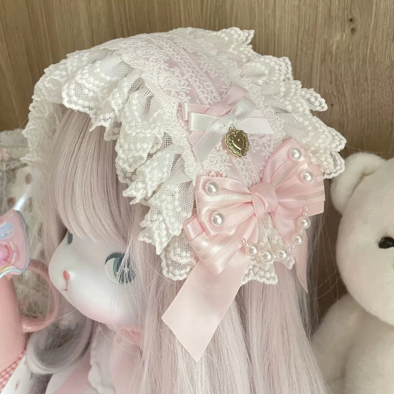 Close-up side view of Sweet Lolita lace bonnet hairband worn on doll, delicate ruffled white lace, large pink satin bow with pearl trim, gold heart charm and long satin ribbon tails
