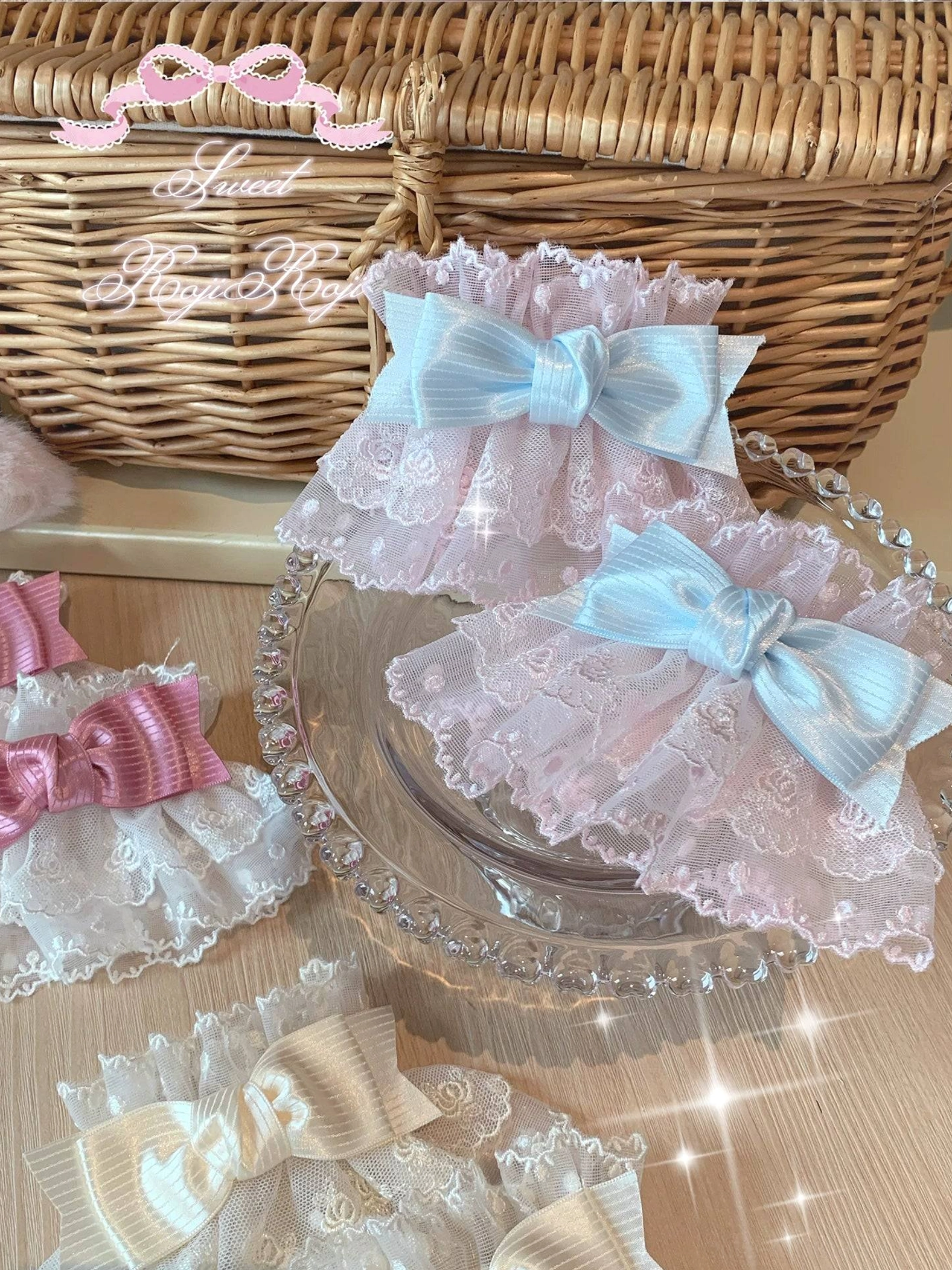Lolita lace bow wrist cuffs oblique overhead display view showing three color options with layered ruffle lace trim on woven rattan basket