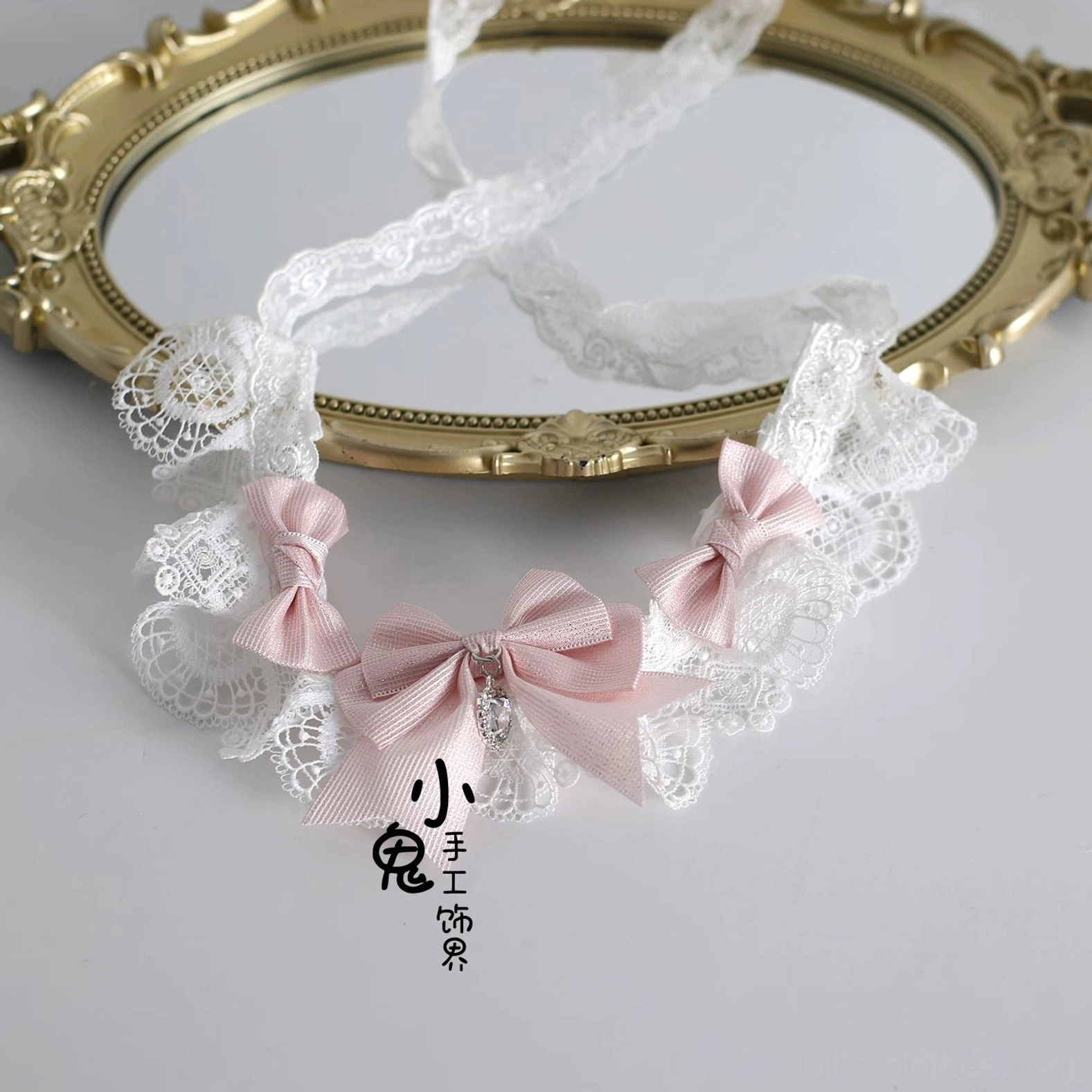 White lace Lolita choker with pink satin bow details and matching hair clips set, displayed on vintage gold decorative mirror, flat lay view