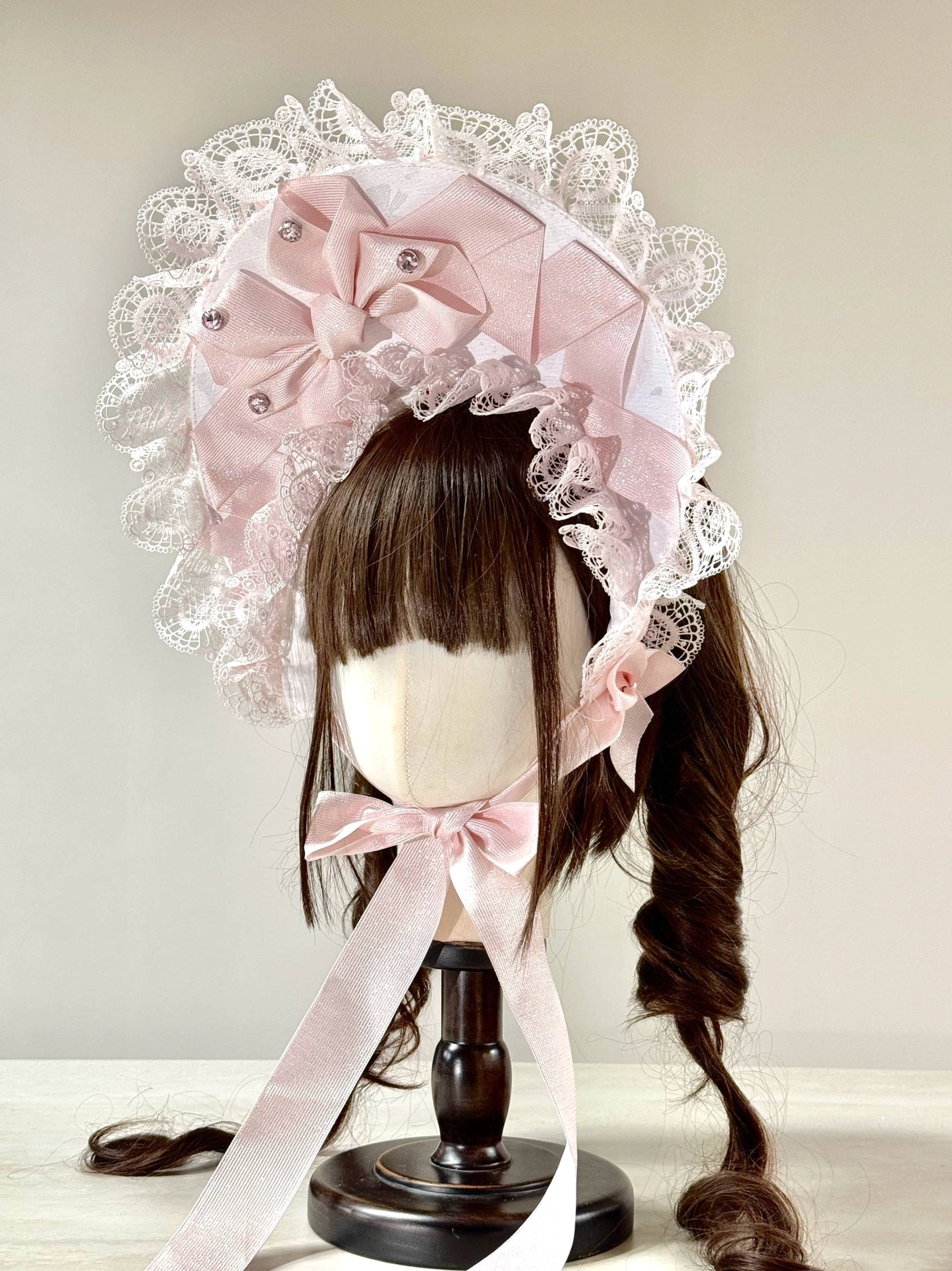 Sweet Lolita lace head bonnet featuring white base, light pink satin bows, sparkling rhinestone accents, delicate ruffled lace edging, matching pink neck ribbons, and pearl decorations