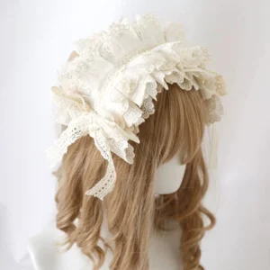 Sweet lolita embroidered lace headdress with tassel bow on blonde wig mannequin, left three-quarter view showing cream white multi-layered ruffled design with side bow details and hanging tassels