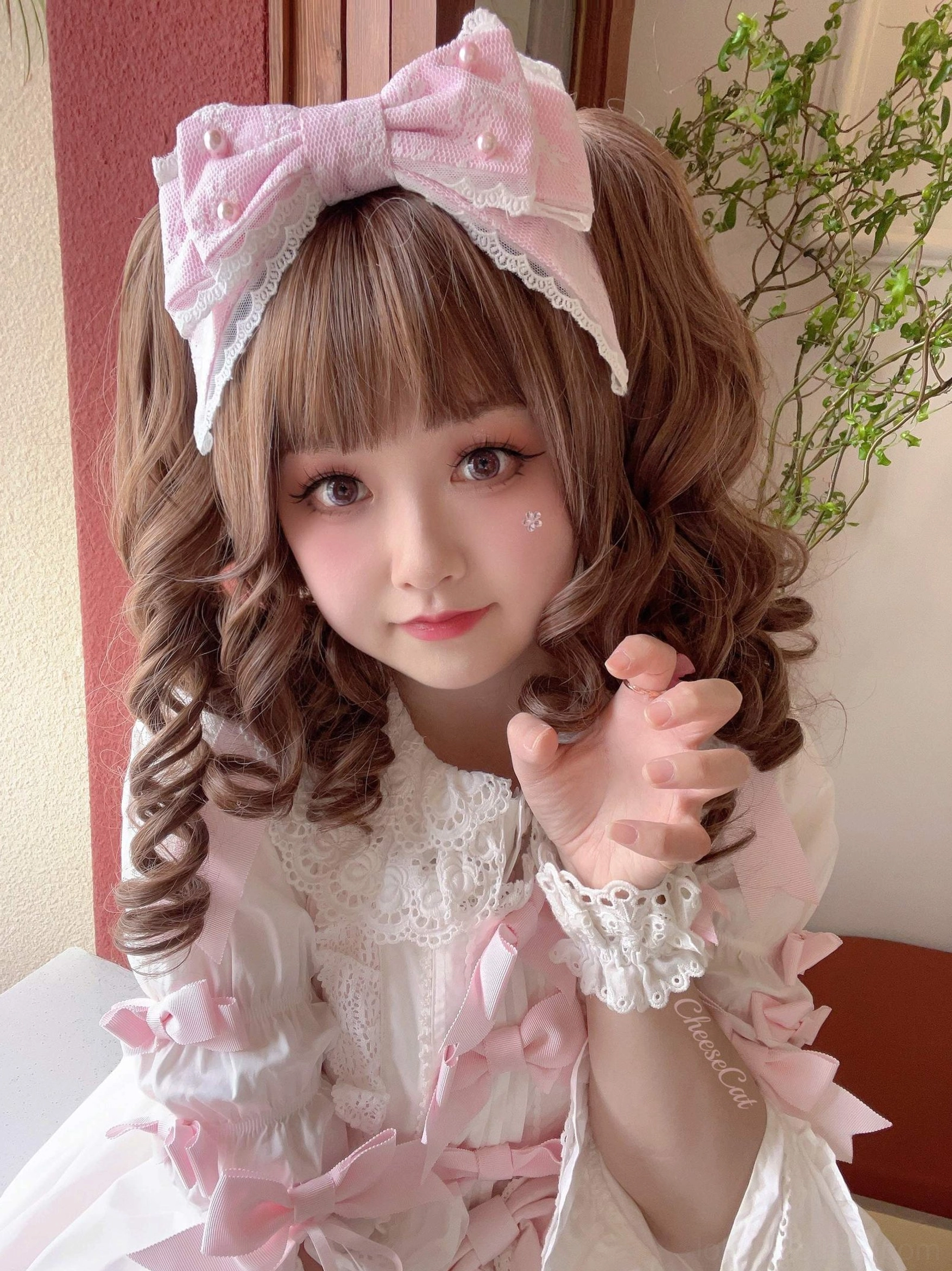 Light pink sweet lolita pearl-trimmed bow KC hair clip worn on real model with brown curly twin hair and pink lolita dress indoor green plants