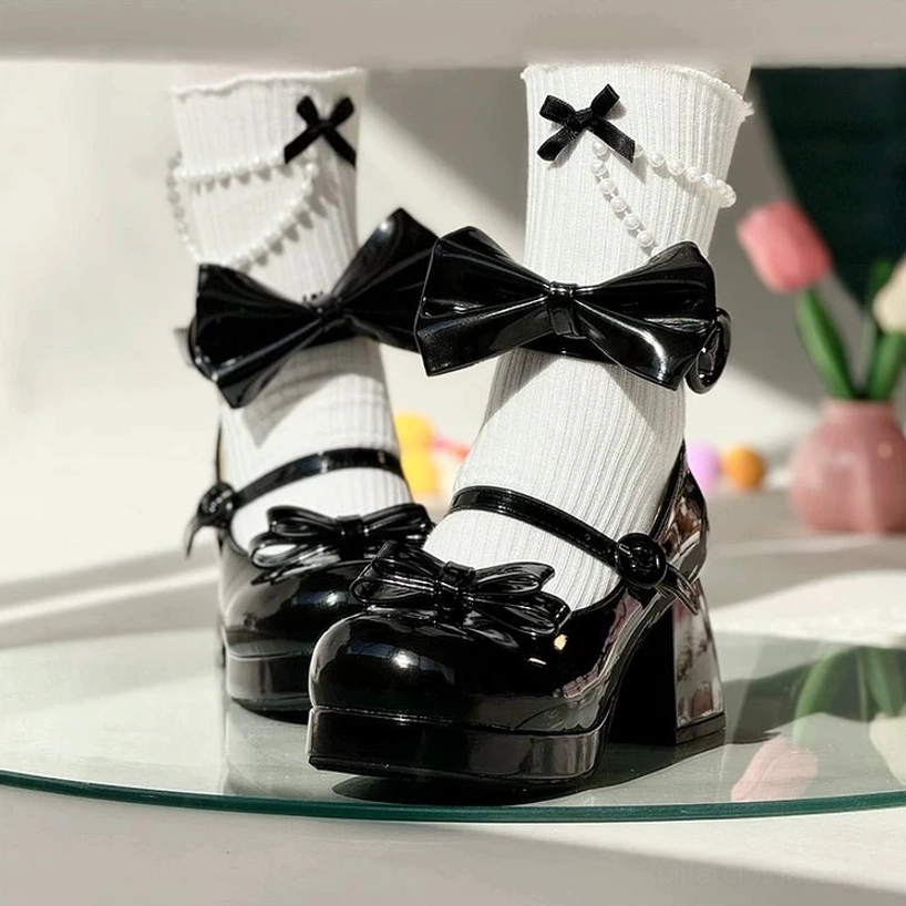 Black patent leather sweet lolita chunky heel mary jane shoes with large detachable bow displayed on glass tray