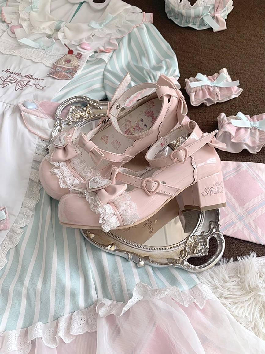 Overhead flat lay view of pink patent leather sweet lolita mary jane heels with lace bow embellishments on silver mirror tray with matching small hair bows and lolita dress fabric