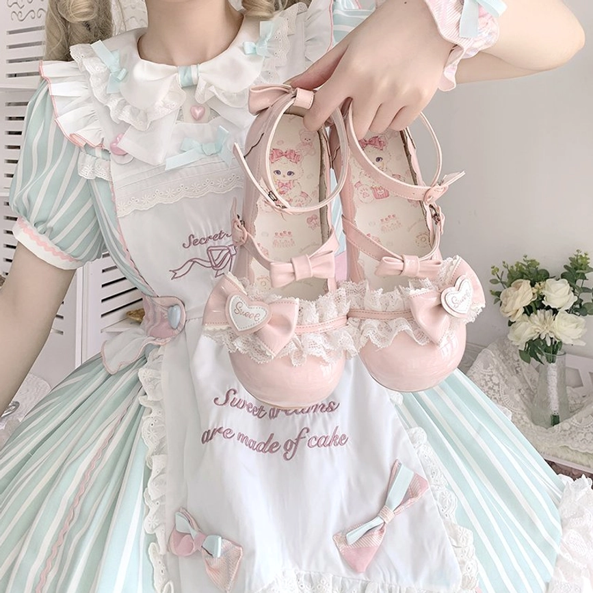 Hand-held close-up angle of sweet lolita mary jane heel shoes featuring lace bow heart decoration patent leather finish ankle strap closure with matching mint pink lolita dress background