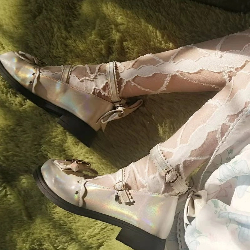 Side close-up view of holographic iridescent sweet lolita shoes worn with ruffled sheer lace socks on green fuzzy background showing star hardware and heel bow