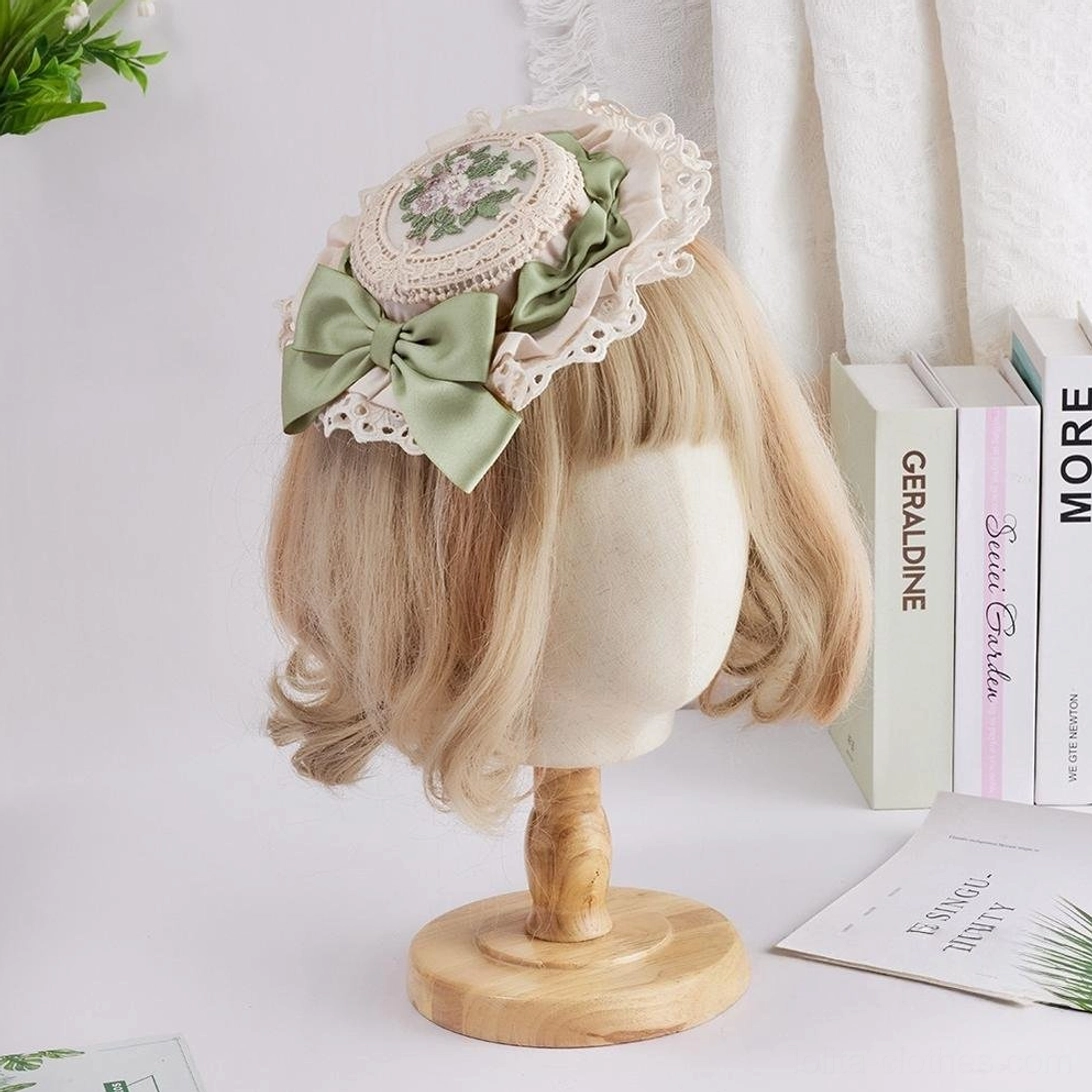 Romantic Sweet Lolita top hat with sage green satin bow, intricate white ruffled lace trim, and hand-embroidered round floral medallion centerpiece