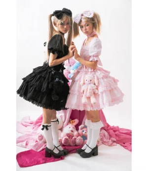 Matching sweet lolita one-piece dresses in black and pink with tiered ruffled skirts, puff sleeves, and coordinating hair bows worn by two models with studio props and Mary Jane shoes