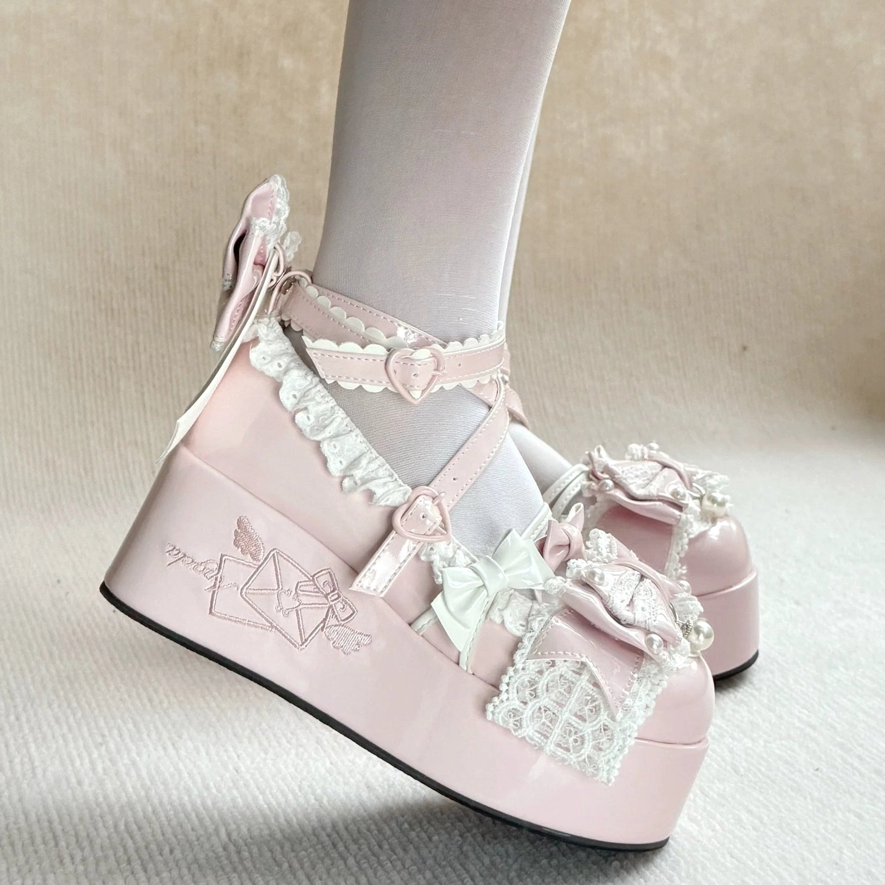 Light pink Sweet Lolita platform heels side on-foot profile showing heart-shaped strap buckle, delicate lace trims, embroidered envelope platform detail, small heel bowknot, white sheer hosiery