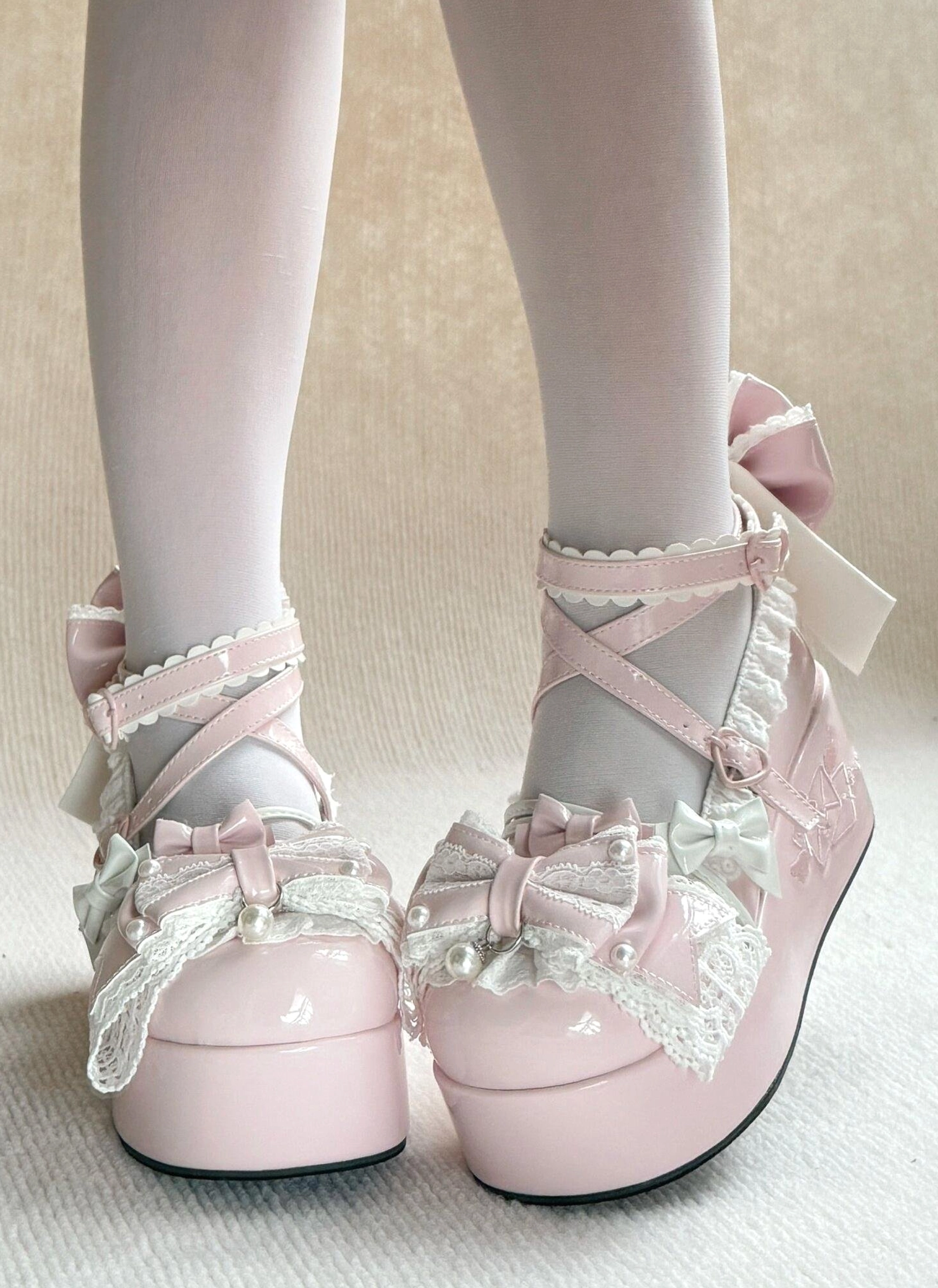 Pink Sweet Lolita high platform shoes on-foot front view with crisscross ankle straps, ruffled lace trim, pearl embellished bowknot, and glossy patent leather upper worn with white sheer stockings