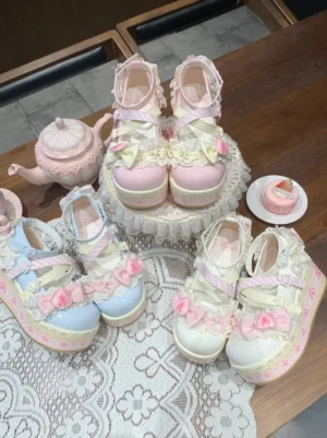 Sweet lolita platform shoes overhead flat lay display featuring three color variants with bows and floral appliques arranged on retro lace placemat with pink teapot and dessert