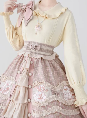 Sweet Lolita puff sleeve knit undershirt with ruffled doll collar in beige-yellow paired with pink plaid skirt featuring rabbit embroidery and layered ruffles, accessorized with pink bow brooch and heart-shaped belt buckle, front upper-body close-up view