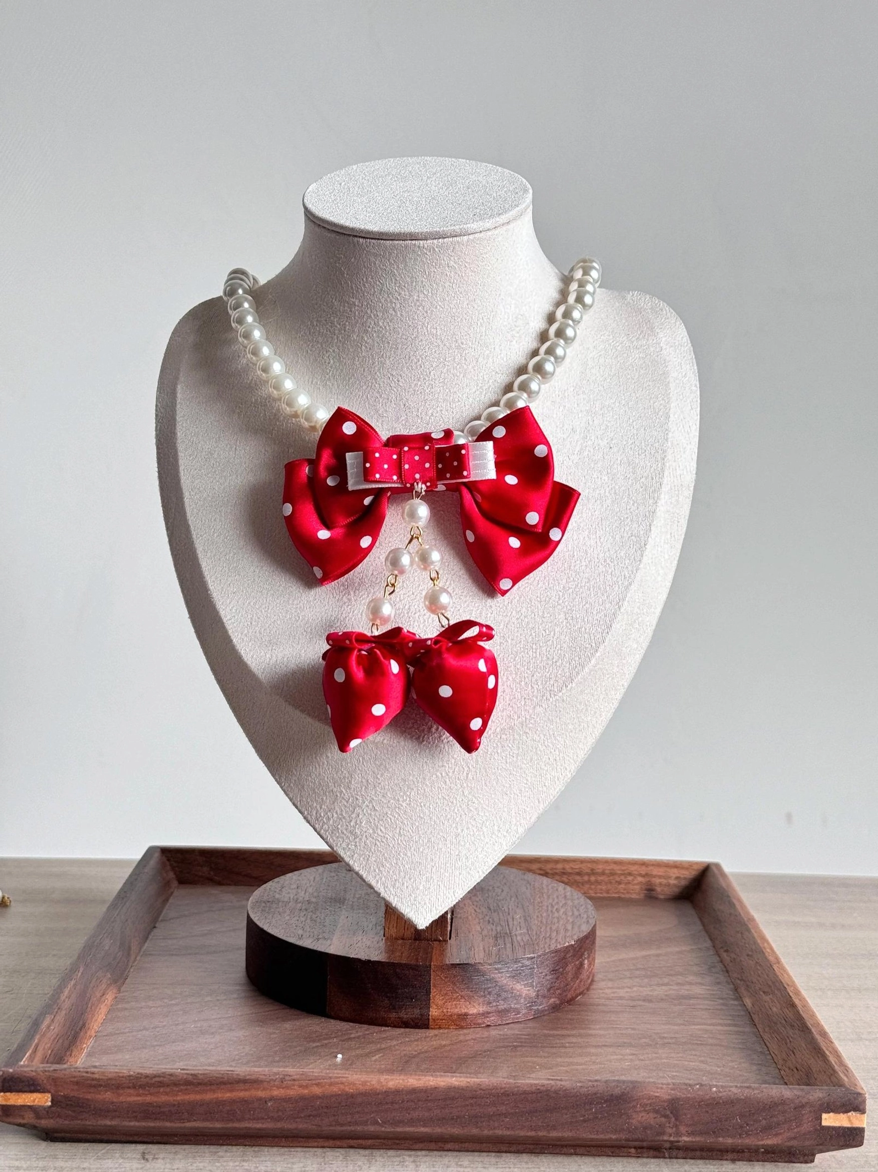 Red sweet lolita polka dot bow pearl choker necklace with dangling pendant on jewelry display stand wooden background