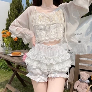 Sweet lolita summer coordinate featuring voluminous ruffled bloomers with delicate lace trim satin bow accents paired with matching cream lace camisole and sheer cardigan outdoor garden setting