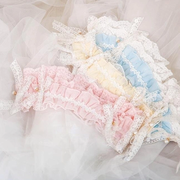 Flat lay close-up view of set of 3 Lolita ruffled hair bands in pastel colors (pink, cream yellow, and sky blue) with ruffled lace edges and tiny pearl details placed on sheer tulle fabric