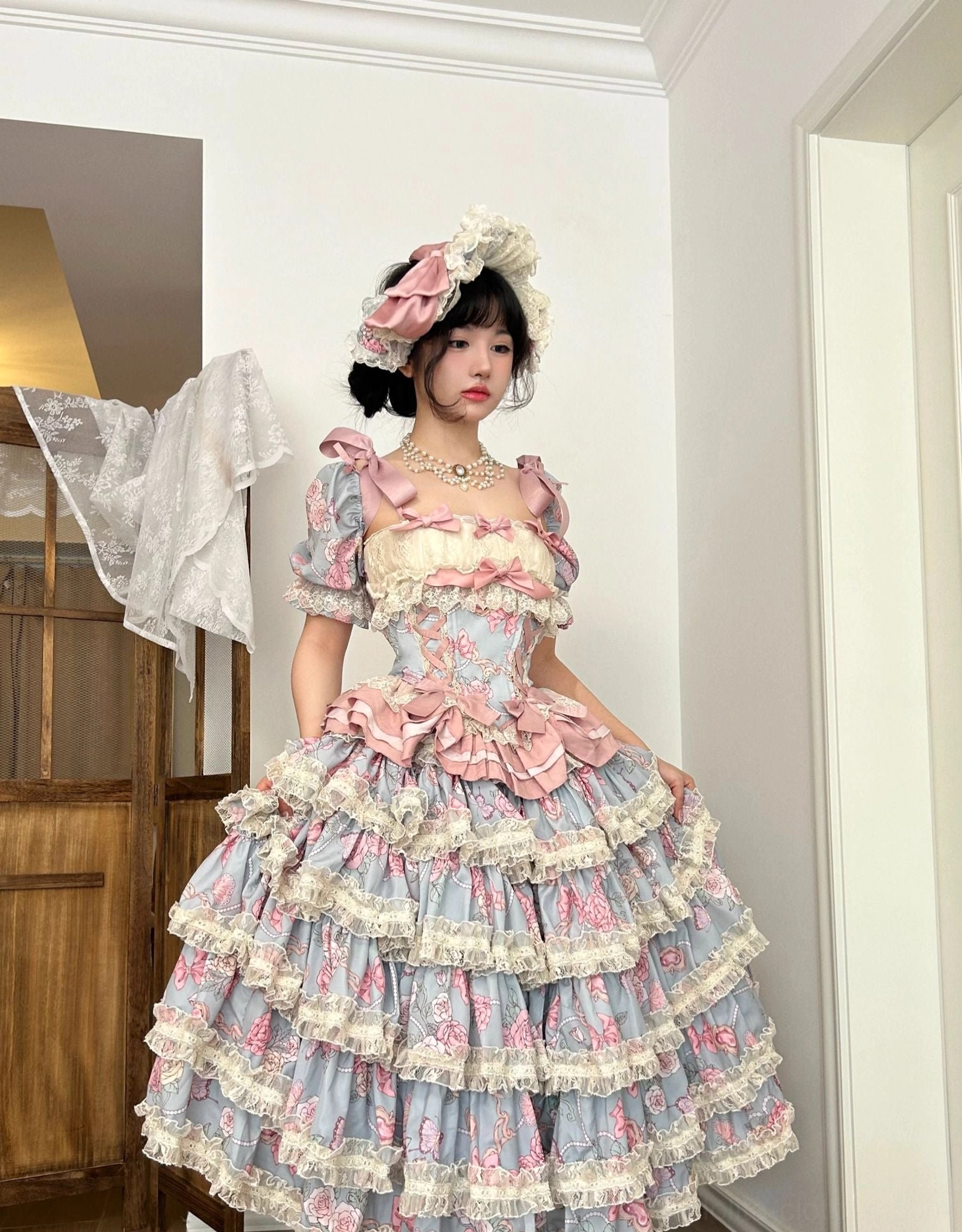 Half-body seated shot of model wearing short-style sweet lolita dress set on bedroom bed showing tiered ruffle short skirt matching pastel color scheme and lace trim details