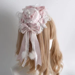 Sweet Lolita small top hat with white lace and pink satin bow, back three-quarter view on blonde wig mannequin, featuring pearl tassels and fluffy pom-pom accents