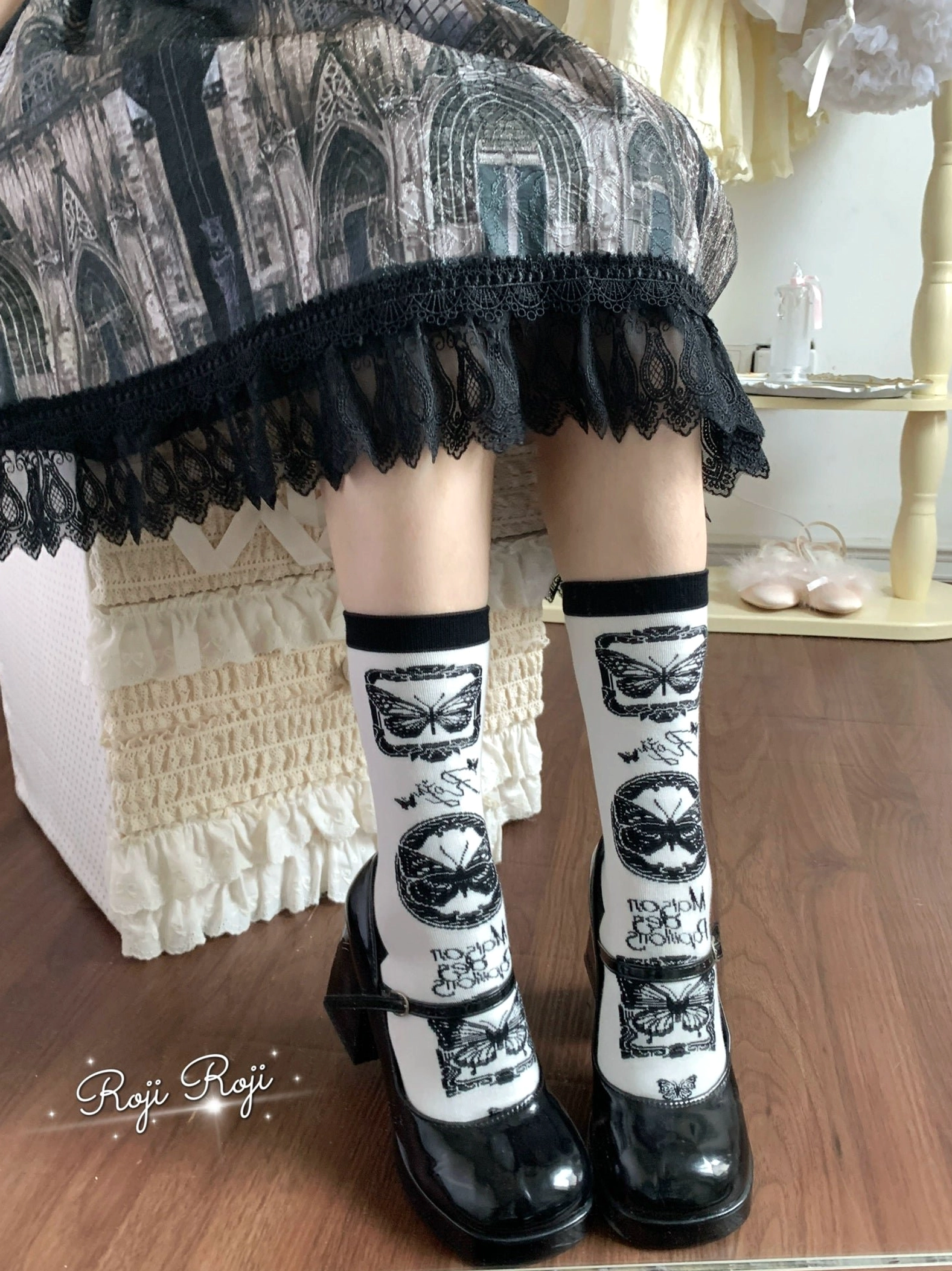 Black and white retro print Sweet Lolita mid-calf cotton socks with butterfly and portrait motifs, worn with black lace-trimmed Lolita skirt and black patent leather flats in vintage room