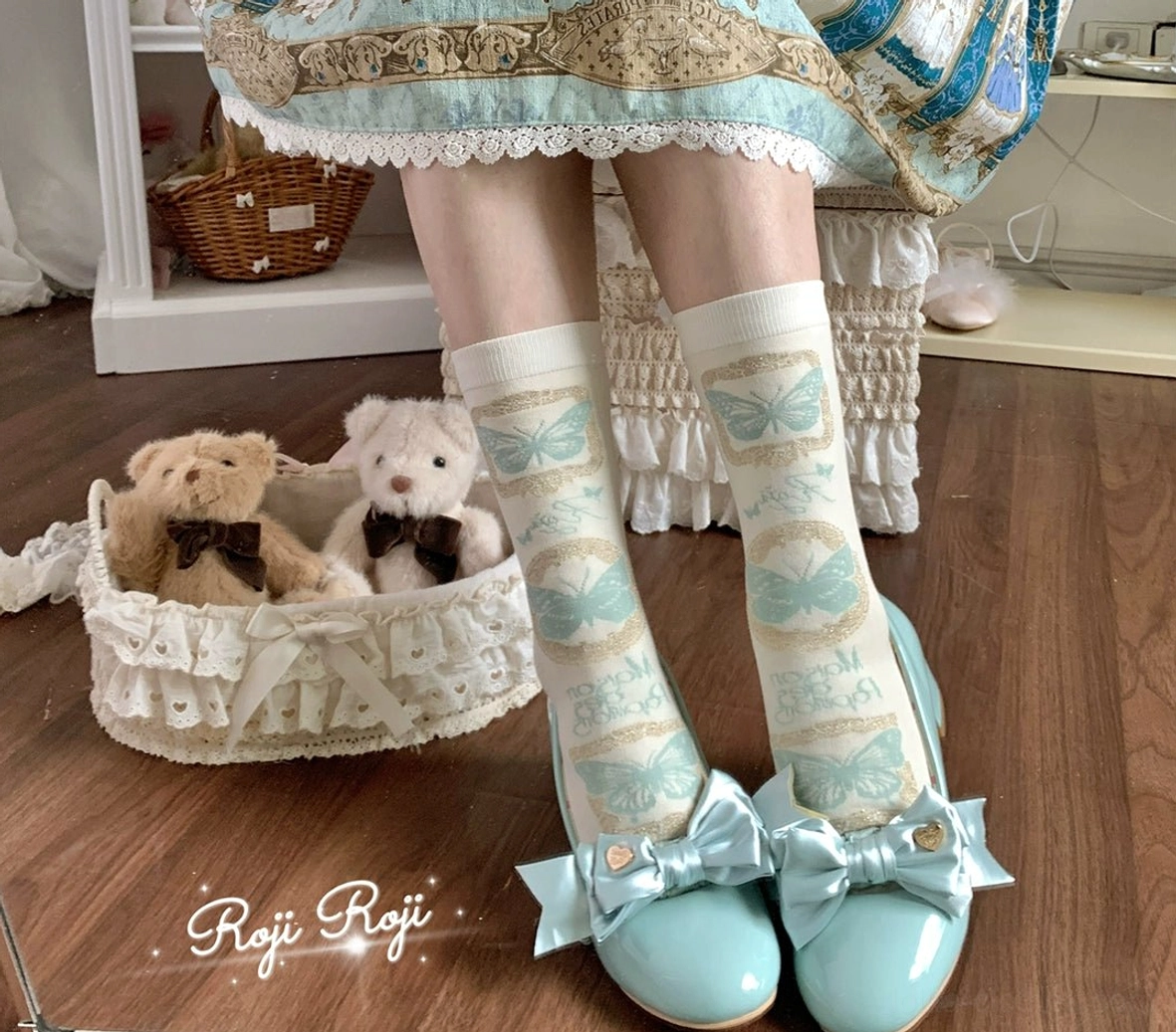 Blue butterfly print Sweet Lolita mid-calf cotton socks with cream base worn with matching blue bow flat shoes and printed Lolita skirt in vintage home setting with plush toys