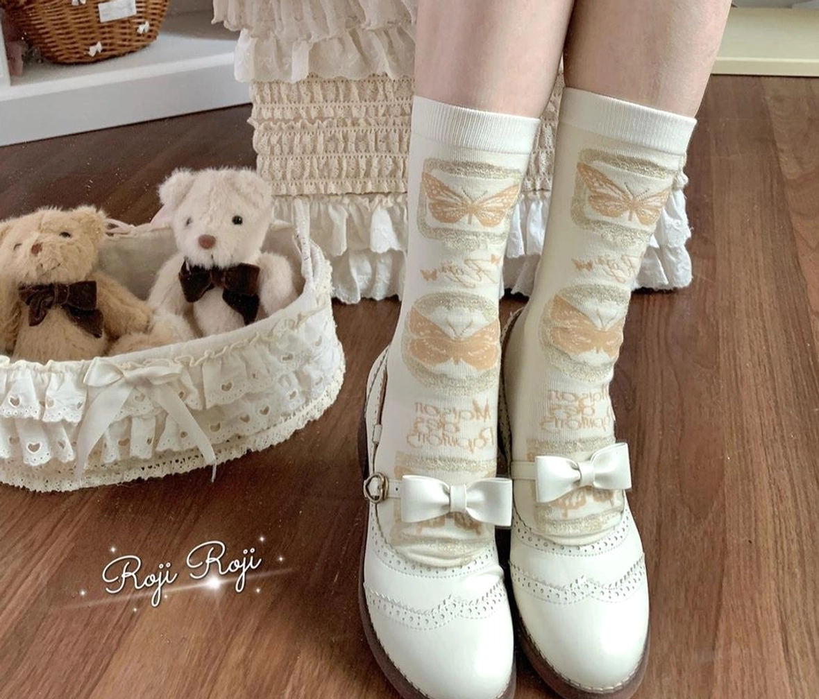 Gold butterfly print Sweet Lolita mid-calf cotton socks with cream base ruffled cuff bow details, worn with Lolita skirt and white bow Mary Jane shoes among plush toys