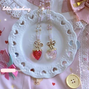 Sweet lolita strawberry charlotte necklace in red and pink resin flat lay on heart-shaped white ceramic plate with decorative gold bow accents and delicate beaded chain details