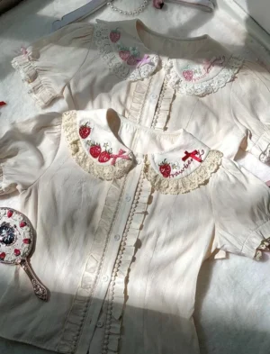 Sweet Lolita strawberry embroidery blouse flat lay top view cream white fabric with lace Peter Pan collar and red strawberry floral embroidery details vintage mirror styling