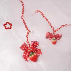Handmade sweet lolita strawberry necklaces overhead flat lay featuring two variants with red link chains, red star charms, pearl accents, polka dot bow and gingham bow designs on white tulle background