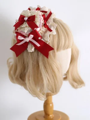 Sweet lolita triangle cake hair headdress with cream lace ruffles and red satin bows displayed on blonde curly wig mannequin from back overhead view