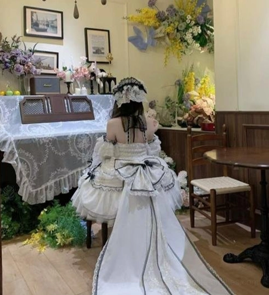 Back view of sweet lolita wedding dress showing long detachable train, large satin waist bow and lace-trimmed hair bonnet in vintage dining room with floral decor
