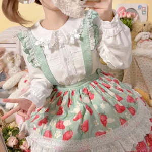 Sweet Lolita coordinate featuring white Peter Pan collar blouse with strawberry print overskirt and suspender details, model wearing twin pigtails in cozy bedroom setting