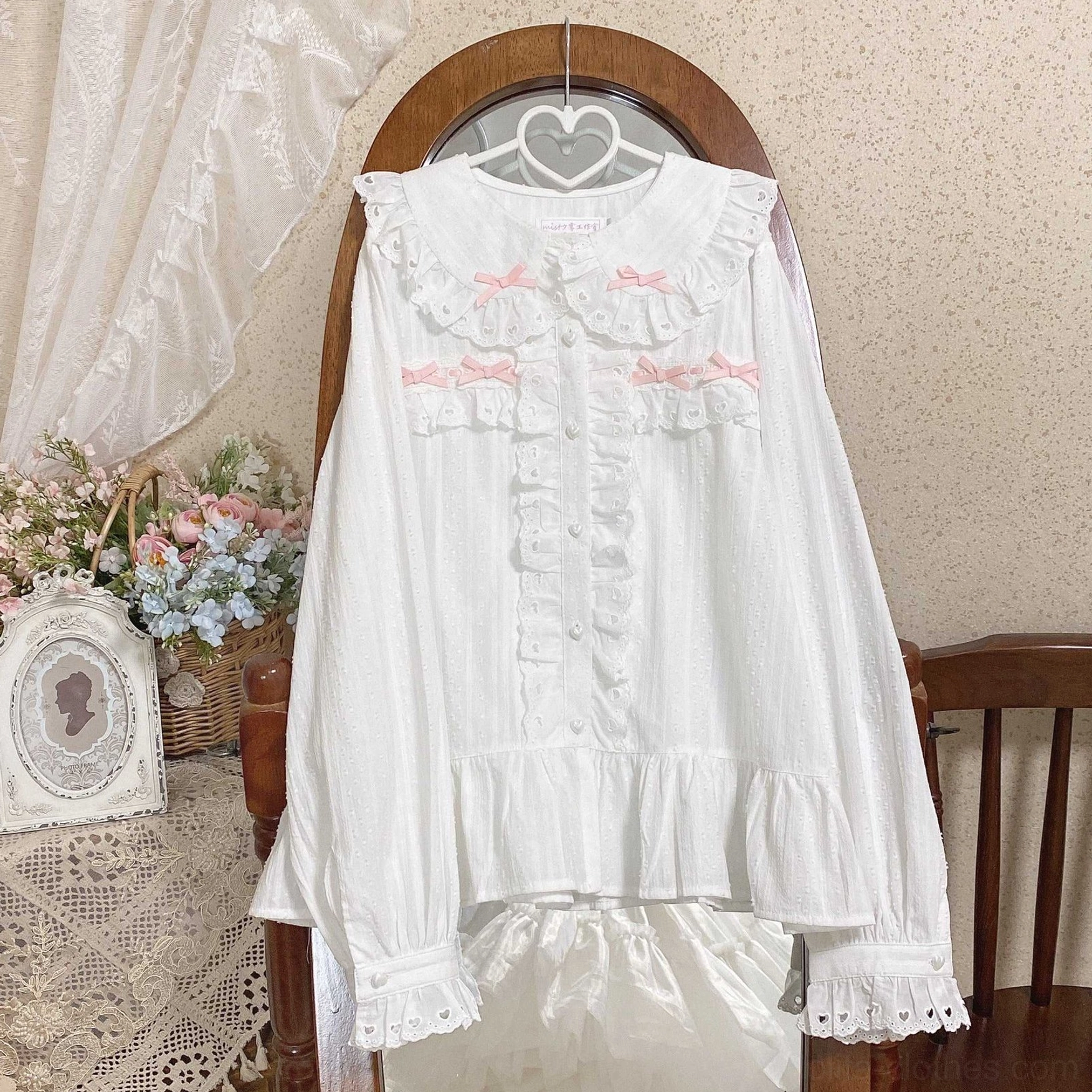 White and pink sweet lolita doll collar blouse with pink chest bows and lace-trimmed cuffs front view hanging display