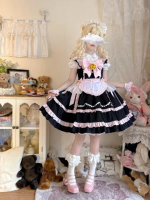 Black and pink Sweetheart Chef sweet lolita JSK dress with oversized golden bell bow and detachable heart-shaped apron, full-body front view on model with blonde curls in vintage doll-themed room