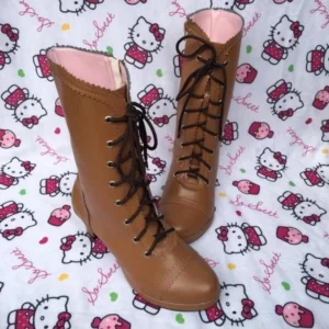 Tan brown Lolita lace-up mid-calf boots featuring pink inner lining, stitched toe cap, and dark brown laces, mixed side and frontal view on Hello Kitty fabric backdrop