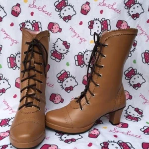 Tan brown Lolita mid-calf lace-up heel boots with scalloped collar and block heel, displayed on Hello Kitty backdrop, showing frontal two-piece product view with smooth leather upper and floral trim details